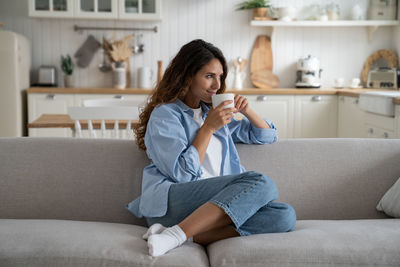 Young woman using phone while sitting on sofa at home