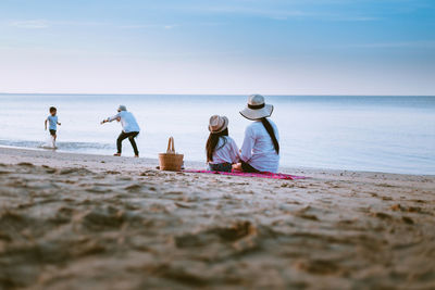 People sitting on beach by sea against sky