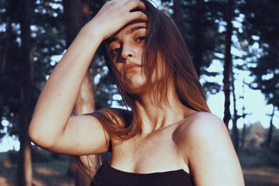 Portrait of young woman with hand in hair against trees