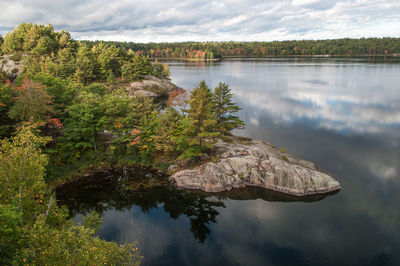 View of rock with trees and lake against cloudy sky