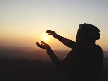 Optical illusion of silhouette man holding sun during sunset