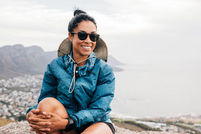 Smiling woman sitting on rock against landscape