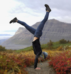 Excited female hiker doing handstand on field against mountains