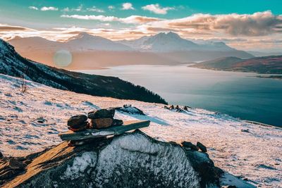 Scenic view of lake by snowcapped mountains against sky during sunset