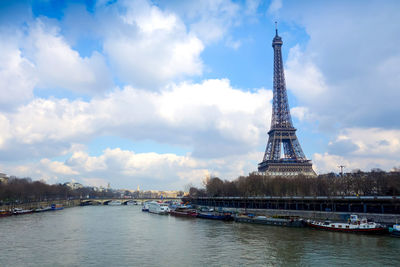 Seine river by eiffel tower against cloudy sky