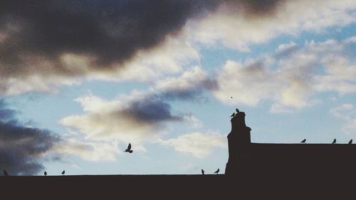 Low angle view of birds perching on cable against cloudy sky