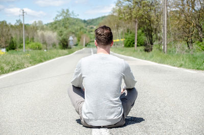 Rear view of man sitting on road during sunny day