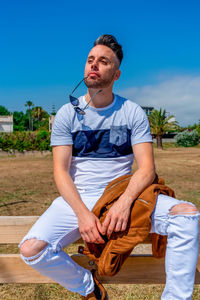 Man sitting on railing against blue sky