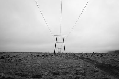 Electricity pylon on land against cloudy sky