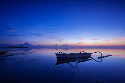 Outrigger canoe at beach against sky during sunset
