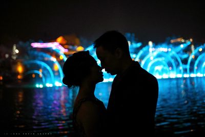 Rear view of friends standing against illuminated light at night