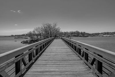 Wooden footbridge leading to water against sky
