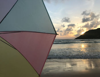 Half scene of sunset on beach with pastel colorful umbrella and sunlight shines on peaceful wave