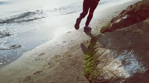 Rear view low section of man jogging on shore at beach