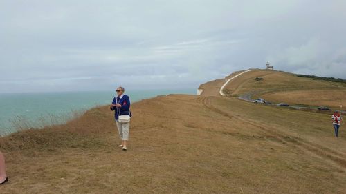 Full length of woman standing on cliff by sea against cloudy sky