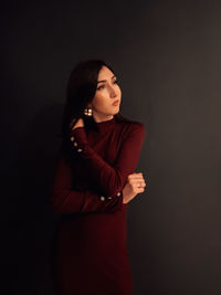 Young woman looking away while standing against black background