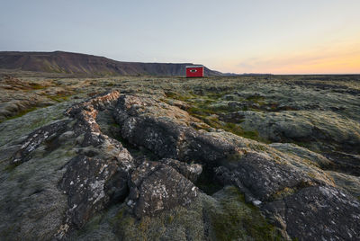 Scenic landscape of rocky location with cabin at sunset