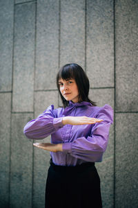 Portrait of young woman gesturing equal sign while standing against wall