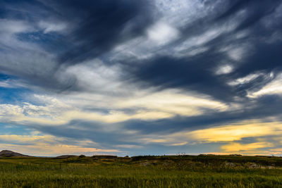 Scenic view of green landscape against cloudy sky during sunset