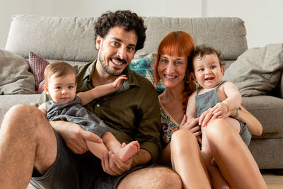 Happy multiethnic young mother and father hugging cute smiling twin babies while sitting on floor during weekend at home