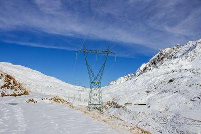 Power line on snowy mountains against sky