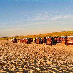 Hooded beach chairs on sand against sky