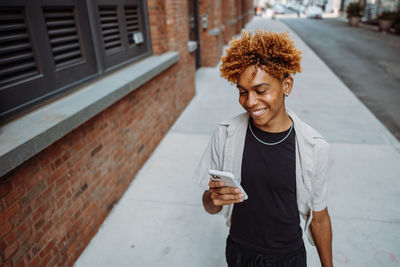 Multiracial guy teenage student using smartphone outdoor on city street while walking alone