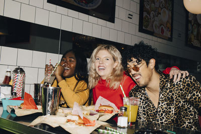 Portrait of happy woman with friends eating burger during social gathering at cafe