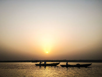 Silhouette boats in sea against orange sky