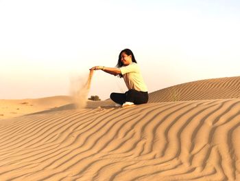 Woman on sand dune in desert against clear sky