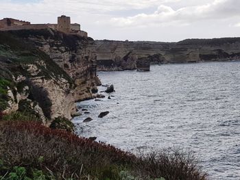 Cliff by sea against sky