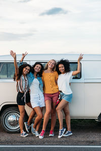 Cheerful female friends standing against camping van on road