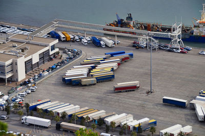High angle view of parked trucks, trailer and cargo container on road by city at commercial dock