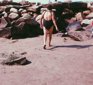 Rear view of woman standing on rock at beach