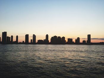 Sea by cityscape against clear sky during sunset
