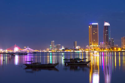 Illuminated buildings by river against sky at night