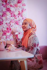 Young woman sitting with pink flower on table