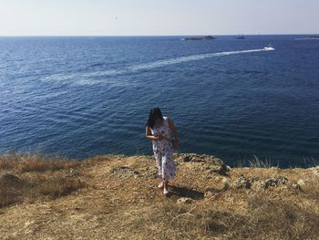 Full length of woman walking on field by sea against sky