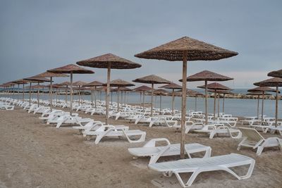 Lounge chairs and parasols on beach against sky