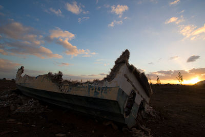 Abandoned boat on field against sky during sunset