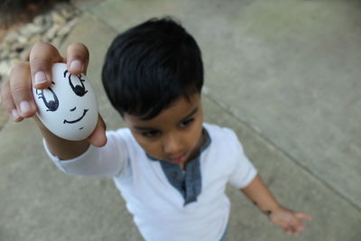 High angle view of boy holding egg with smiley face