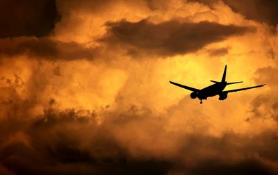 Low angle view of silhouette airplane flying against cloudy sky in stormy weather
