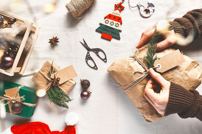 Woman's hands holding christmas gift wrapped in craft paper on the table with christmas decoration.