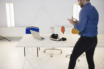 Rear view of male blogger using smart phone while standing at desk in creative office