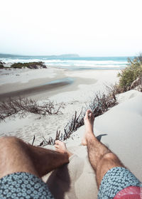 Low section of people on beach against clear sky