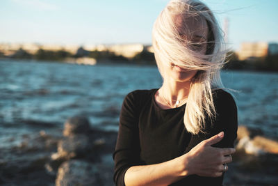 Woman with tousled hair standing against sea during sunset