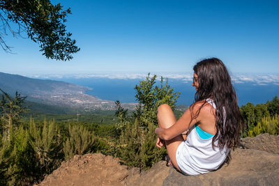 Woman looking at while sitting on mountain against sky