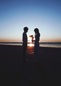 Couple standing on beach against sea against sky