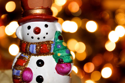 Close-up of snowman figurine against illuminated christmas lights at night