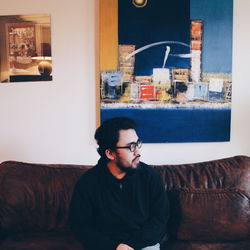 Young man looking away while sitting on sofa